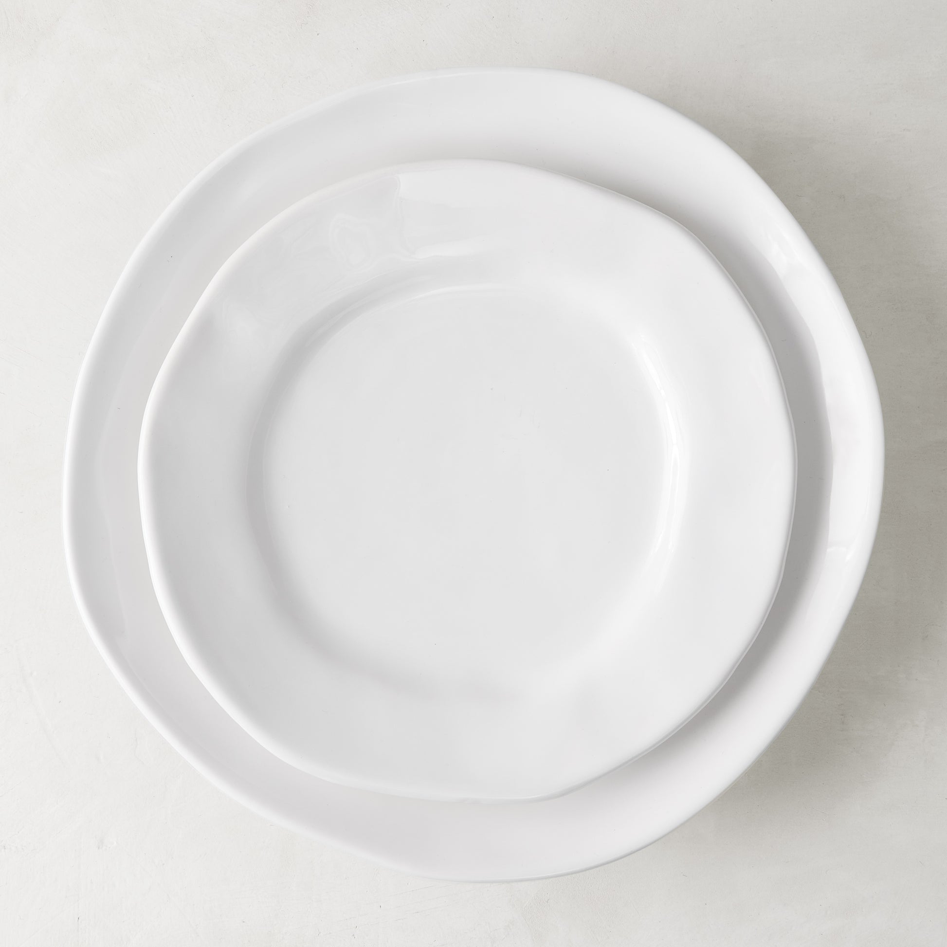Two white ceramic plates with subtle organic edges, the smaller salad plate on top of a larger dinner plate.