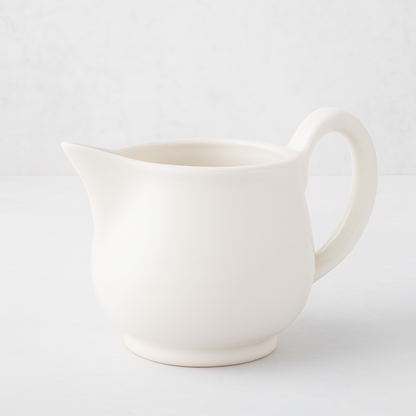 Creamy white ceramic pitcher with a sturdy handle and angled spout.