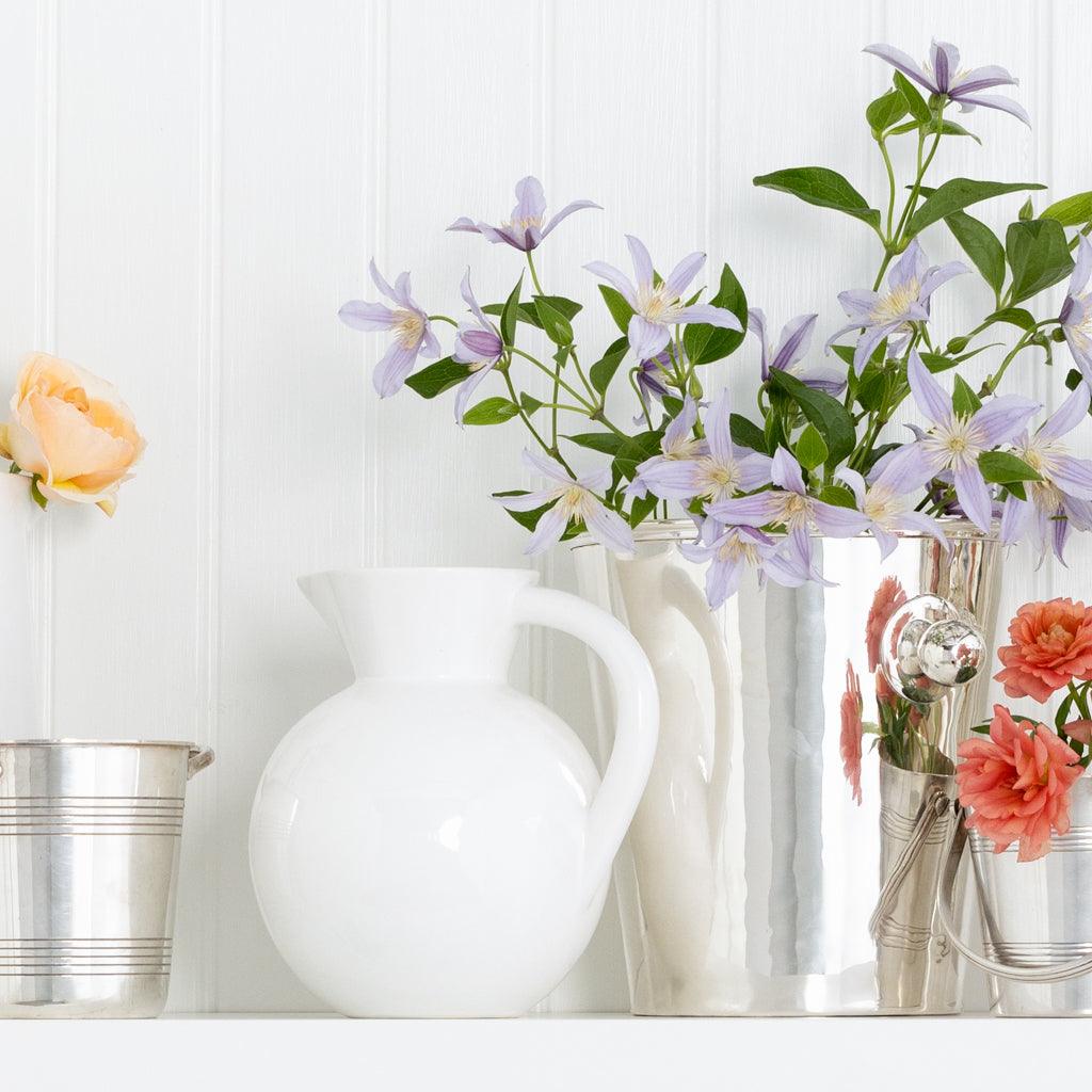 HG Original Small Round Ceramic Pitcher in creamy white, next to silver vases with flowers.