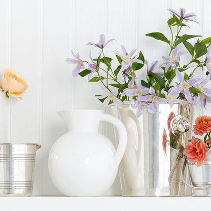 HG Original Small Round Ceramic Pitcher in creamy white, next to silver vases with flowers.