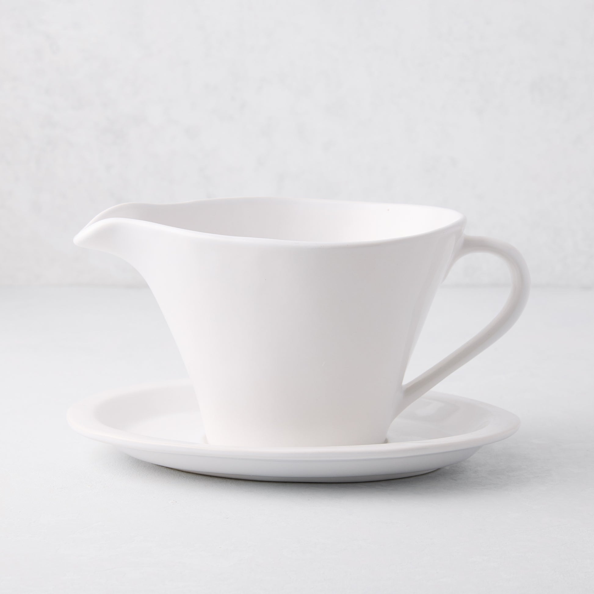 Oversized white stoneware gravy boat with handle, spout, and attached plate.