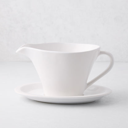 Oversized white stoneware gravy boat with handle, spout, and attached plate.