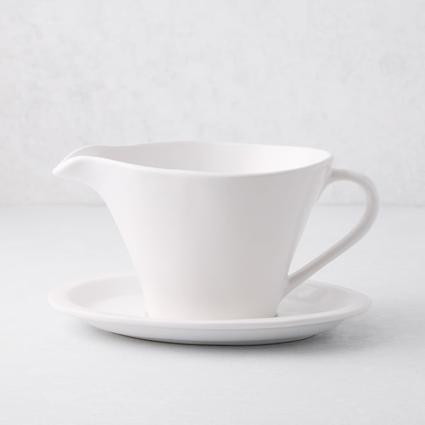 Oversized white stoneware gravy boat with handle, spout, and attached plate.