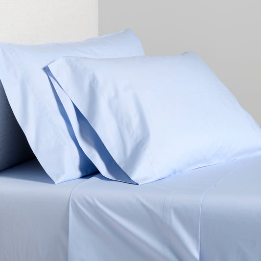 Oxford Blue Italian Percale Sheet Set: light blue cotton flat sheet and two pillowcases on a bed.