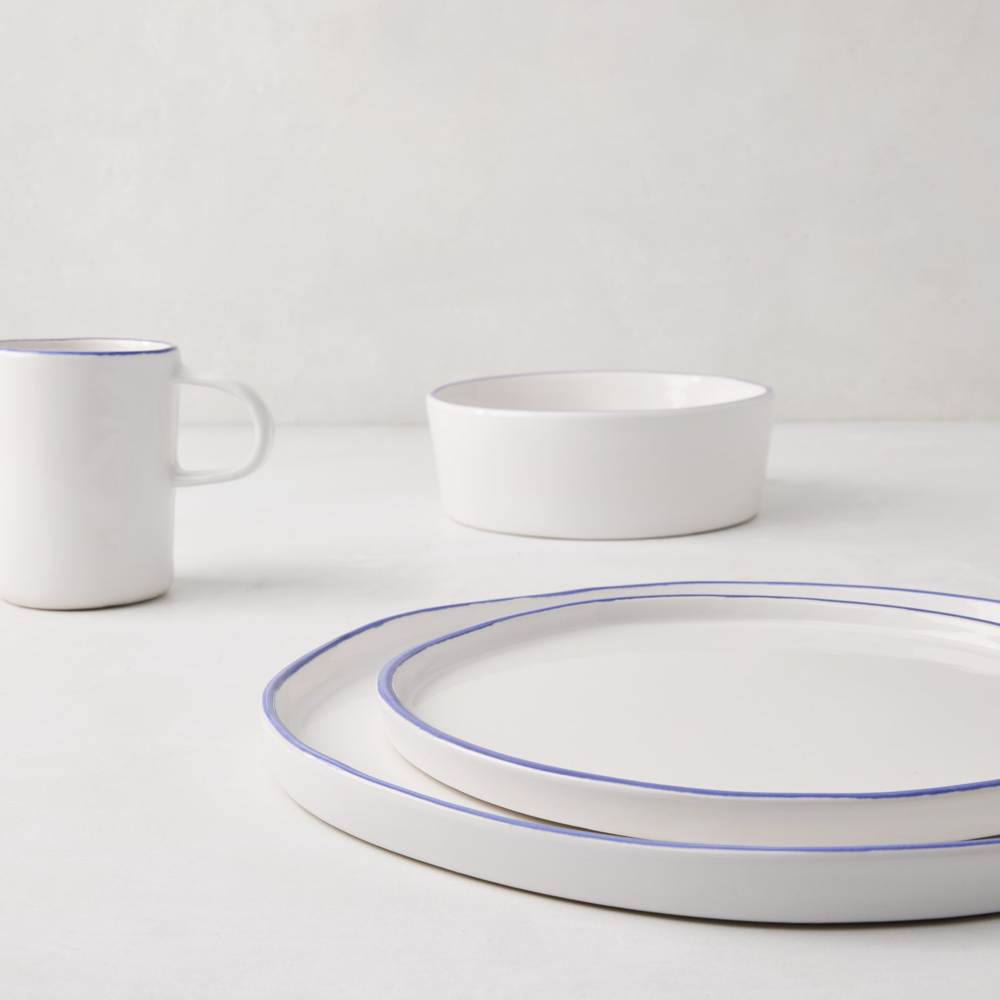 Stacked Pacific Blue-Rimmed Stoneware Dinner Plates, with a matching mug and bowl in the background.