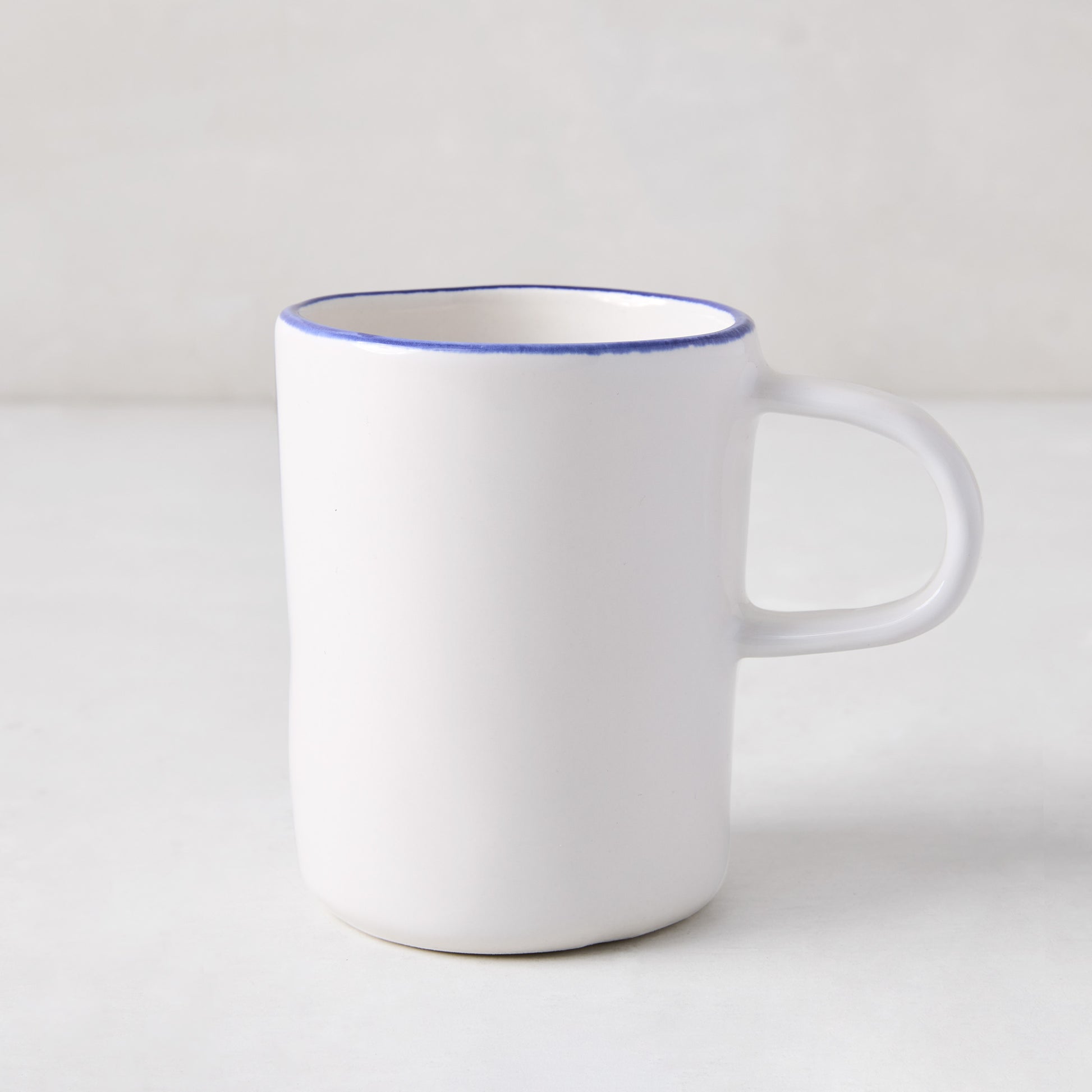 Pacific Blue-Rimmed Stoneware Mug, white with hand-painted blue edge, irregular shape.