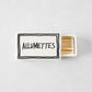 White ceramic match box with hand-drawn black border and Allumettes text, filled with wooden matches.