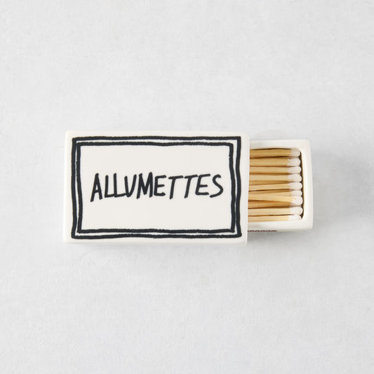 White ceramic match box with hand-drawn black border and Allumettes text, filled with wooden matches.
