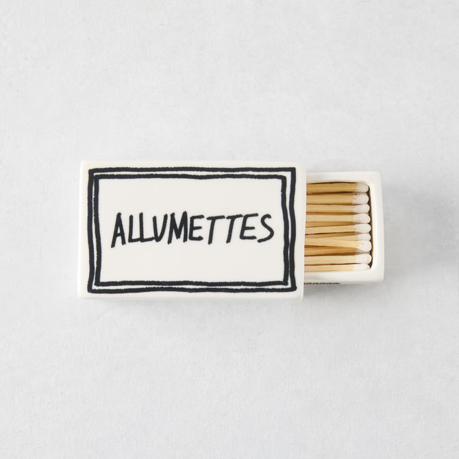 White ceramic match box with hand-drawn black border and Allumettes text, filled with wooden matches.