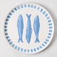 White terracotta round serving platter with three hand-painted blue sardines and a blue border.