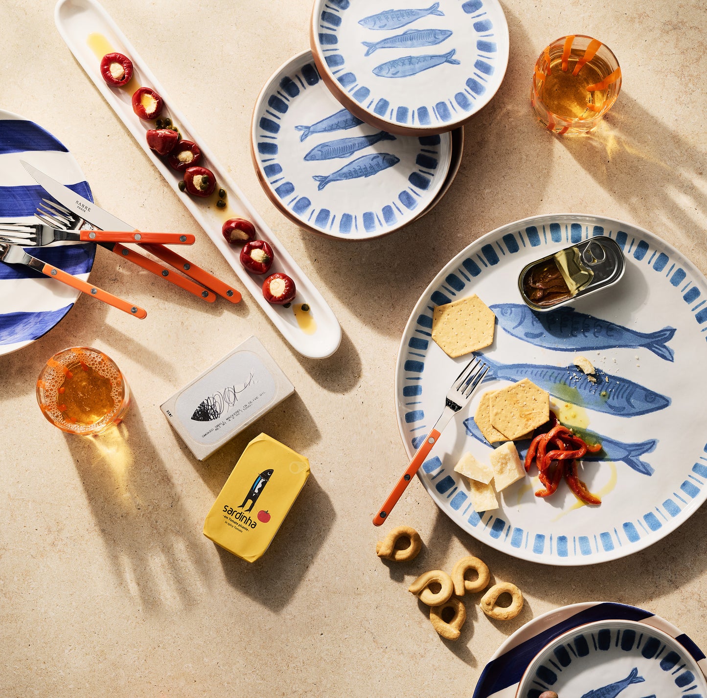 White terracotta salad plate with hand-painted blue sardines and striped rim, set with food and drinks.