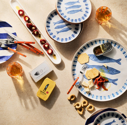 White terracotta salad plate with hand-painted blue sardines and striped rim, set with food and drinks.