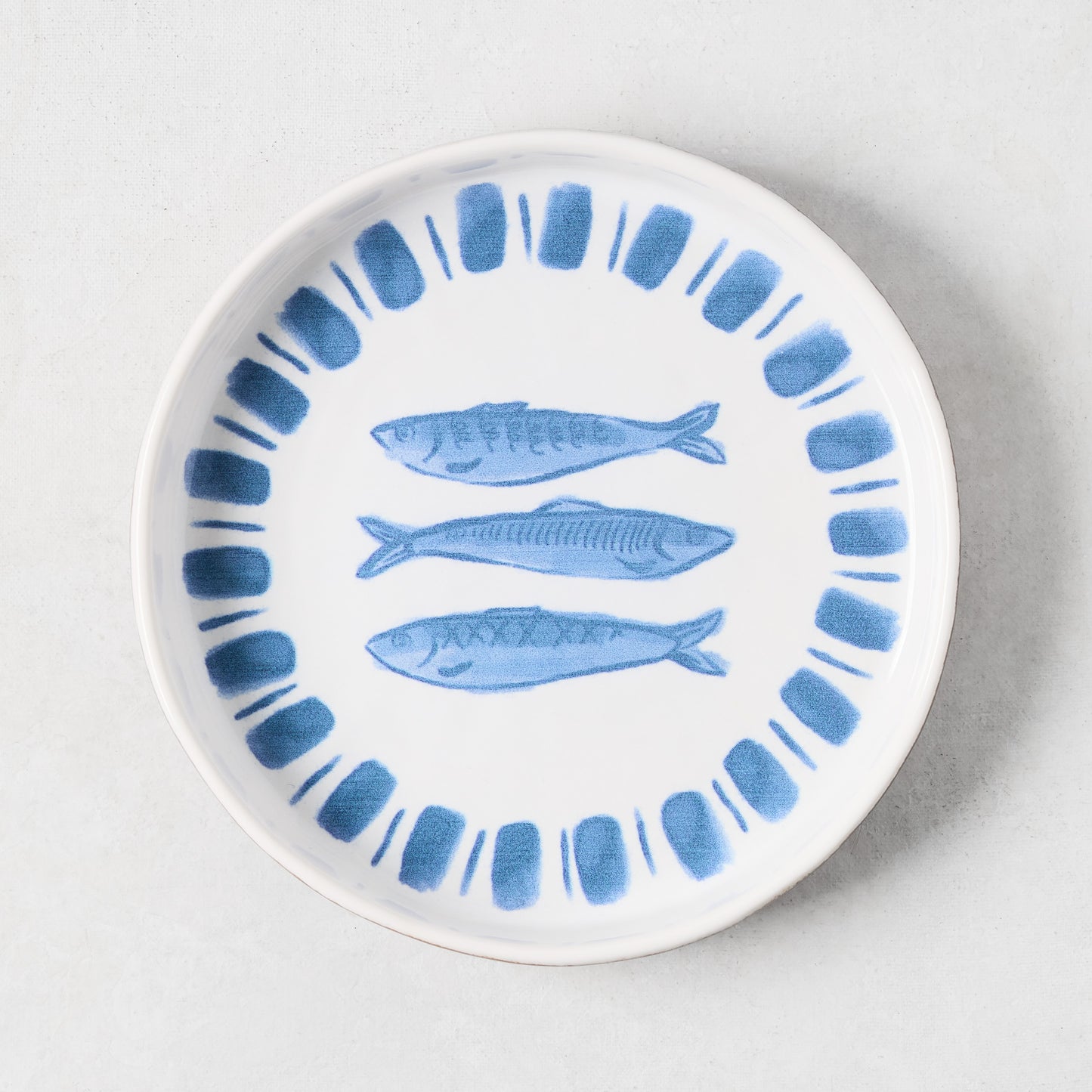 White terracotta salad plate with hand-painted blue sardines and a blue striped rim.