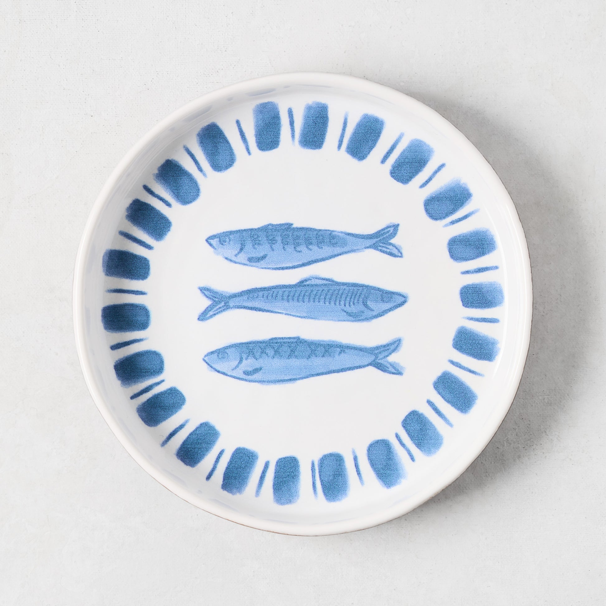 White terracotta salad plate with hand-painted blue sardines and a blue striped rim.