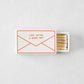 White porcelain match box featuring a red envelope illustration and the text Love Letter I Never Sent, filled with matches.