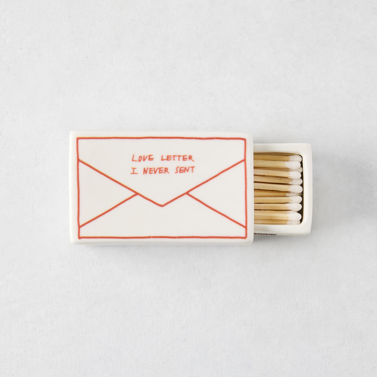 White porcelain match box featuring a red envelope illustration and the text Love Letter I Never Sent, filled with matches.