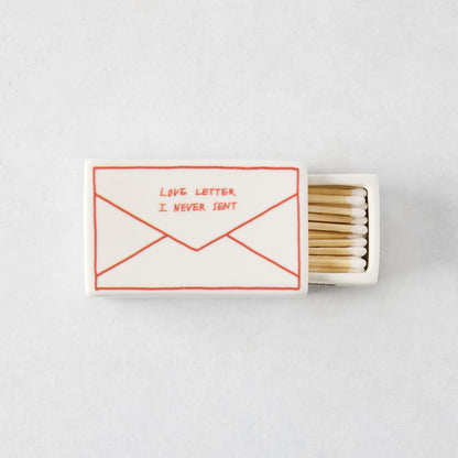 White porcelain match box featuring a red envelope illustration and the text Love Letter I Never Sent, filled with matches.