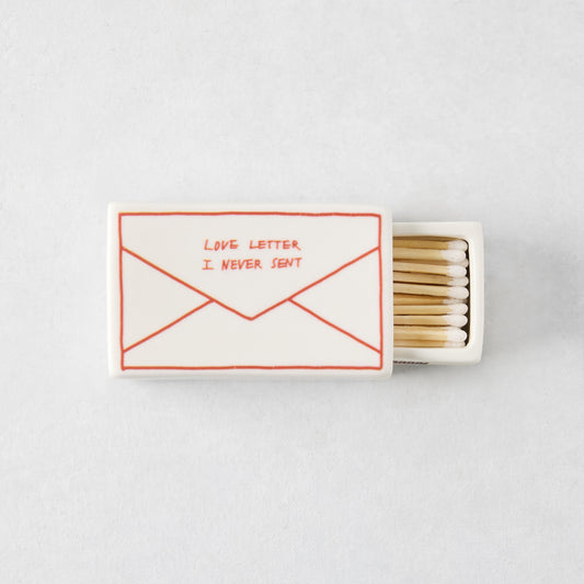 White porcelain match box featuring a red envelope illustration and the text Love Letter I Never Sent, filled with matches.