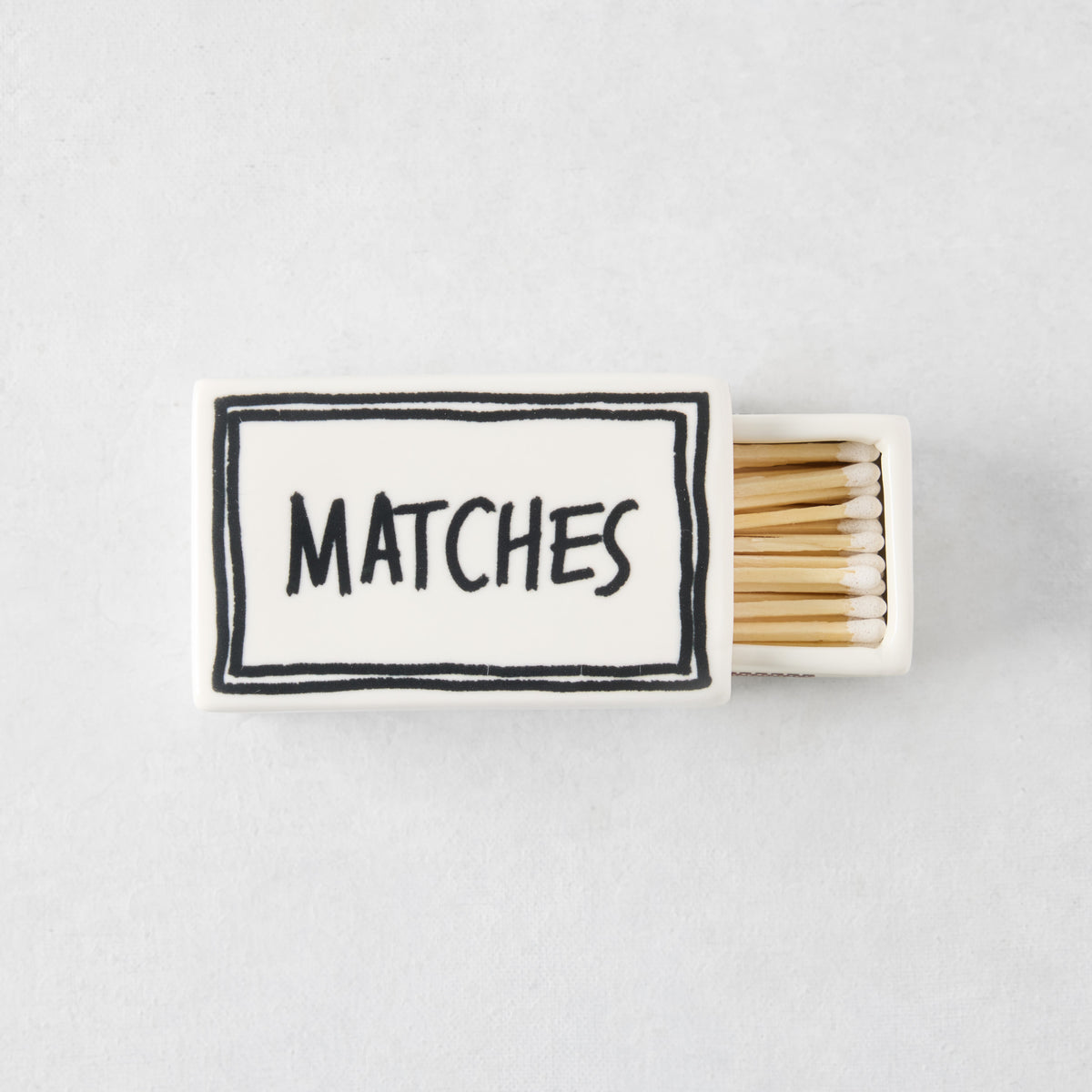 White ceramic matchbox with hand-drawn black border and the word MATCHES, filled with wooden matches.