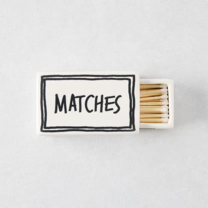 White ceramic matchbox with hand-drawn black border and the word MATCHES, filled with wooden matches.