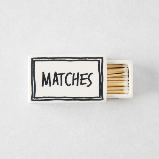 White ceramic matchbox with hand-drawn black border and the word MATCHES, filled with wooden matches.