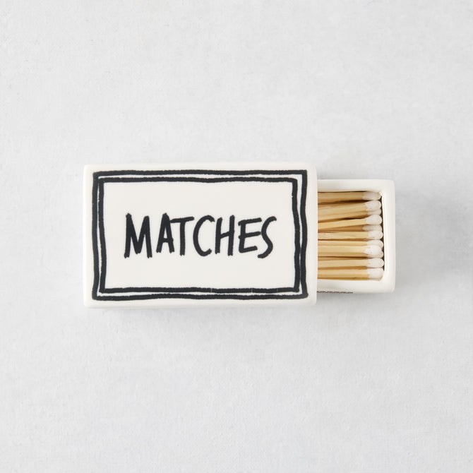 White ceramic matchbox with hand-drawn black border and the word MATCHES, filled with wooden matches.