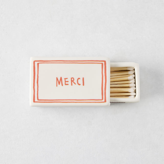White porcelain match box with red border and Merci text, filled with wooden matches, 3.54 by 2.17 inches.