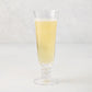 Palermo Stem Champagne Flute, clear hand-blown glass with curved lip and artistic stem, filled with a yellow beverage.