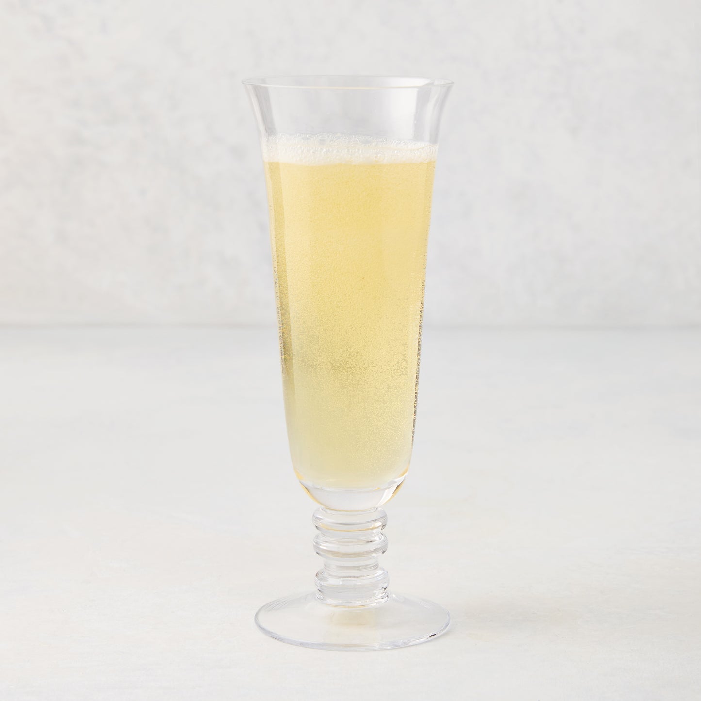 Palermo Stem Champagne Flute, clear hand-blown glass with curved lip and artistic stem, filled with a yellow beverage.