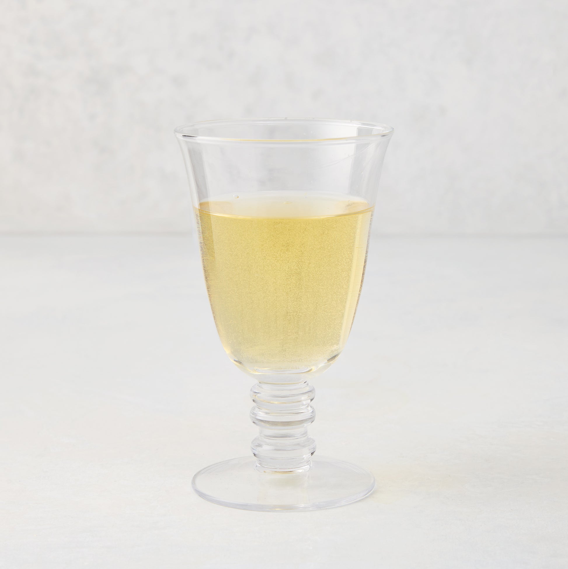 Palermo Stemmed Wine Glass, clear hand-blown glass with a curved lip and artistic ribbed stem, filled with white wine.
