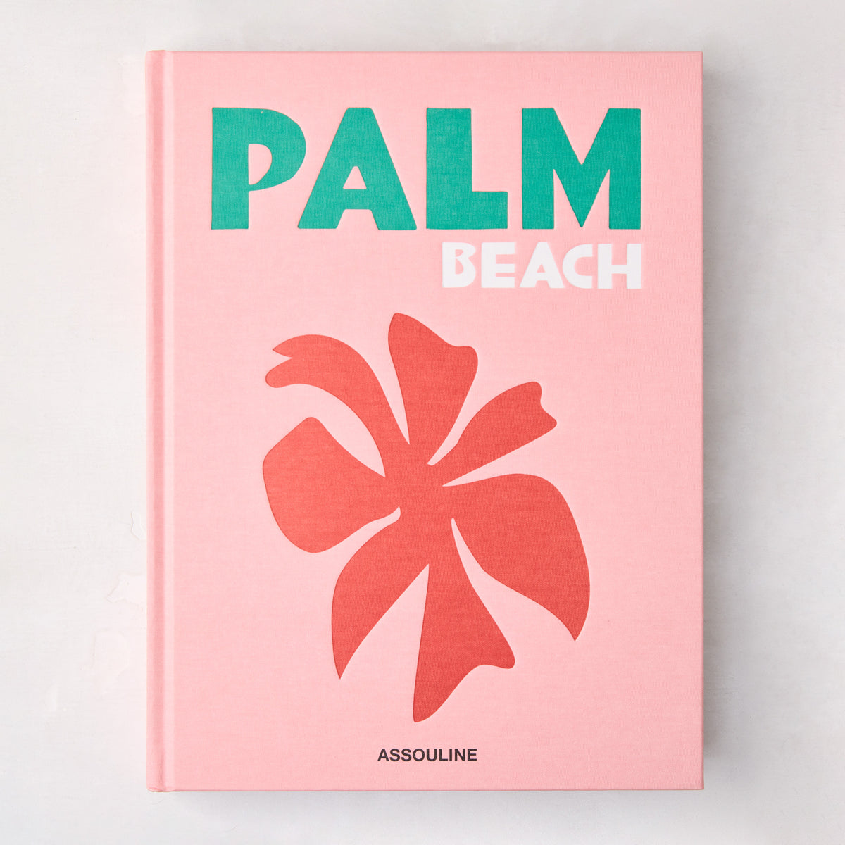 Pink hardcover "Palm Beach" book with green and white title, coral palm leaf graphic, and Assouline logo.