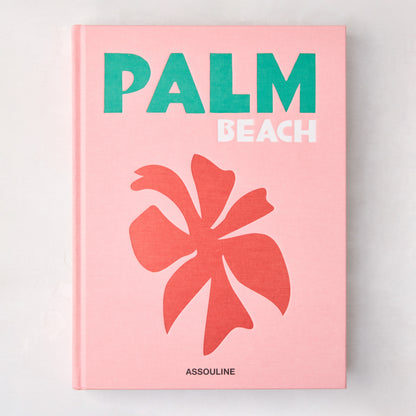 Pink hardcover "Palm Beach" book with green and white title, coral palm leaf graphic, and Assouline logo.