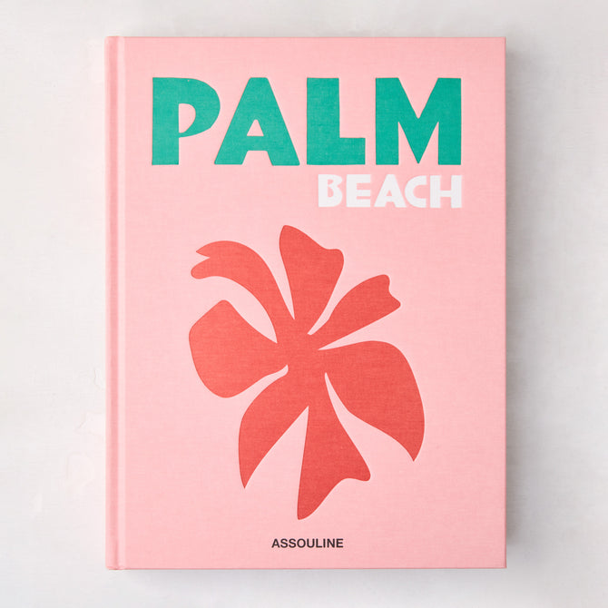 Pink hardcover "Palm Beach" book with green and white title, coral palm leaf graphic, and Assouline logo.