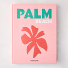 Pink hardcover "Palm Beach" book with green and white title, coral palm leaf graphic, and Assouline logo.
