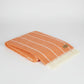Papaya orange Fiji stripe throw blanket, cotton-acrylic blend, with white fringe and brand tag.