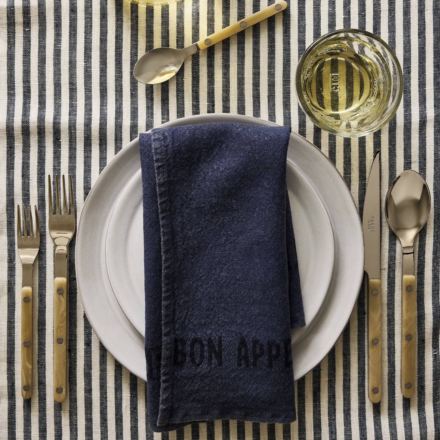 Paris Bistro 5-piece flatware set with stainless steel heads and cream acrylic handles on a striped tablecloth.