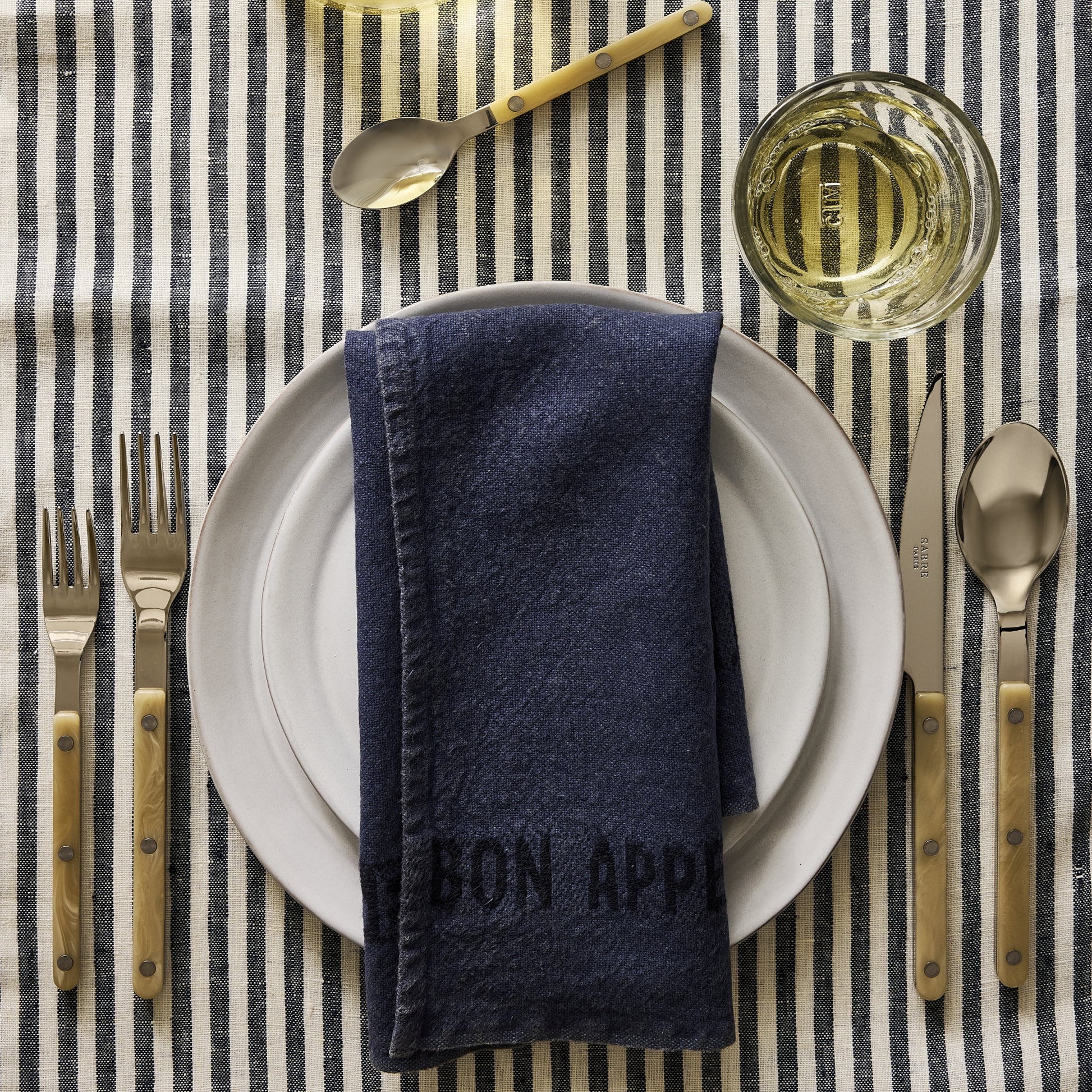 Paris Bistro 5-piece flatware set with stainless steel heads and cream acrylic handles on a striped tablecloth.