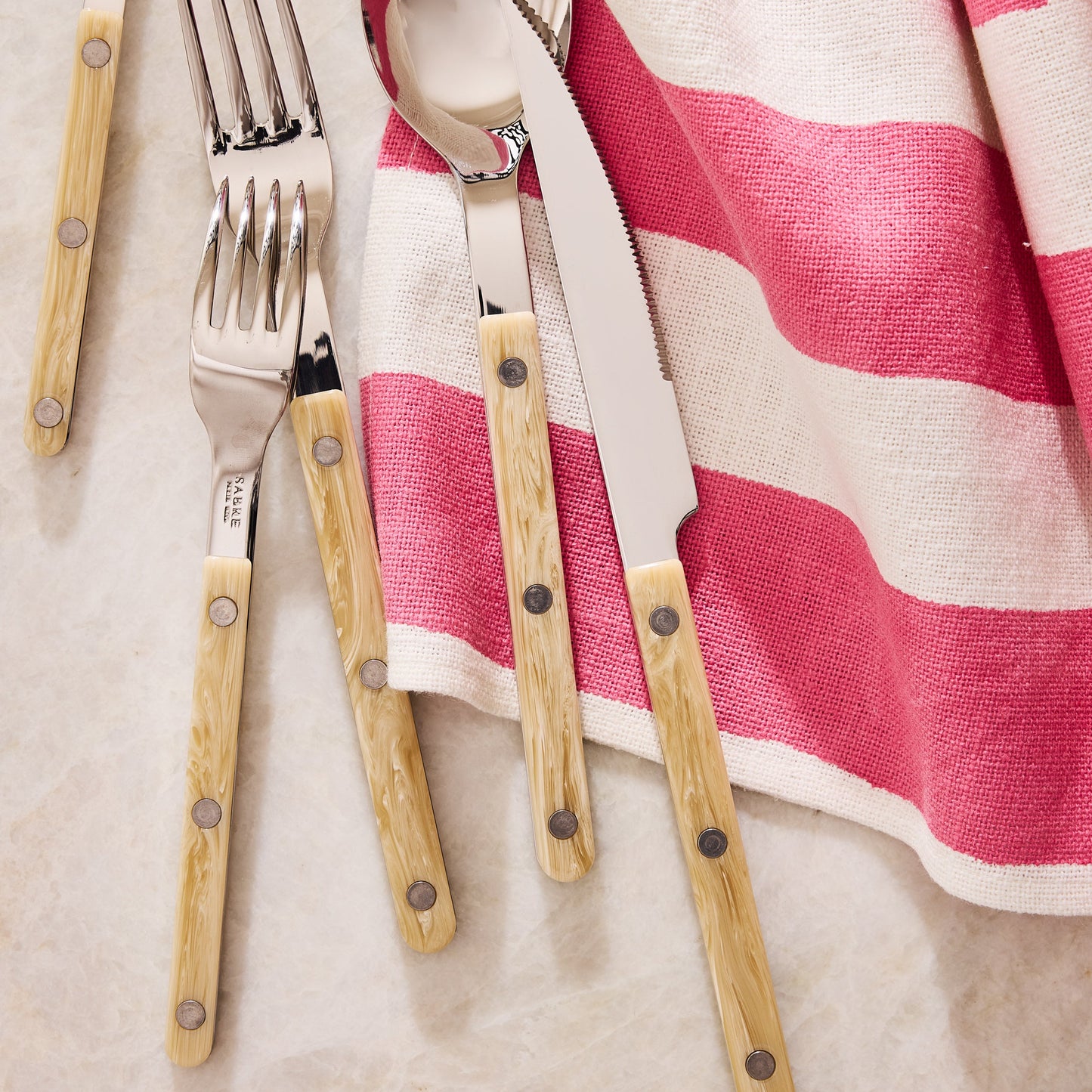 Paris Bistro 5-piece flatware set with stainless steel heads and cream-colored acrylic handles on a striped napkin.