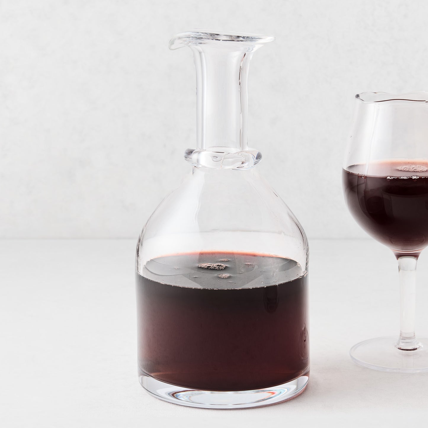 Mouth-blown crystalline glass wine carafe with a wide base, ridged neck, and rippled rim filled with red wine.