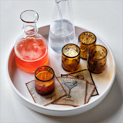 Clear mouth-blown glass Paris wine carafe with a rippled rim on a white tray with amber glasses and cocktail coasters.