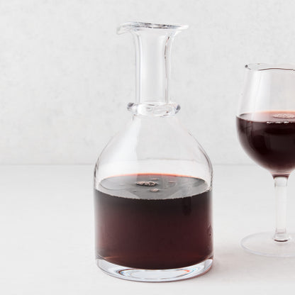 Mouth-blown crystalline glass wine carafe with a wide base, ridged neck, and rippled rim filled with red wine.