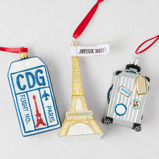 Parisian-themed Christmas ornament set featuring a glittery CDG luggage tag, gold Eiffel Tower, and silver suitcase.