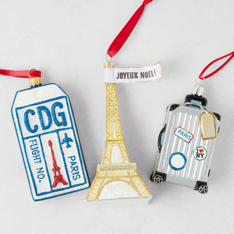 Parisian-themed Christmas ornament set featuring a glittery CDG luggage tag, gold Eiffel Tower, and silver suitcase.