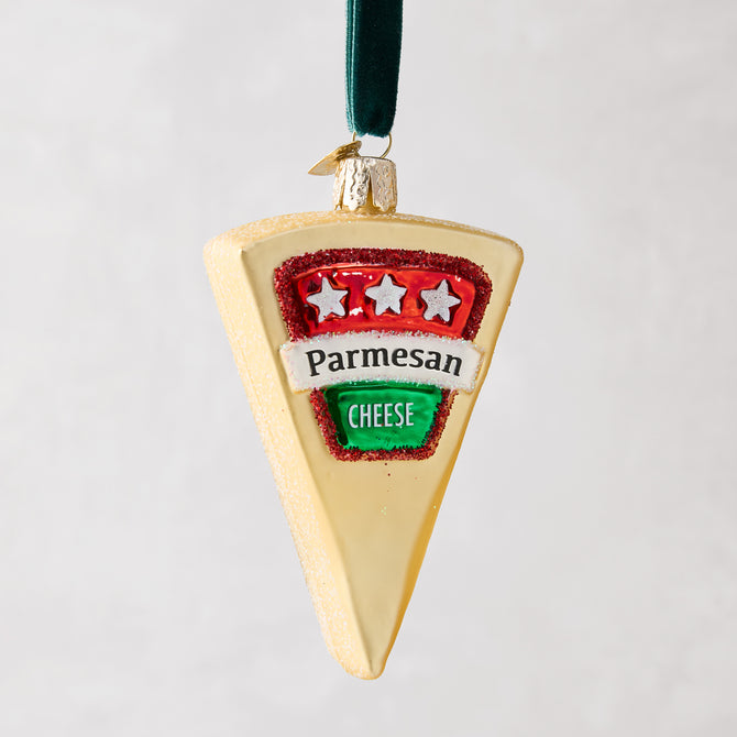 Hand-painted glass Parmesan cheese wedge Christmas ornament with glitter, red and green label, and velvet ribbon.