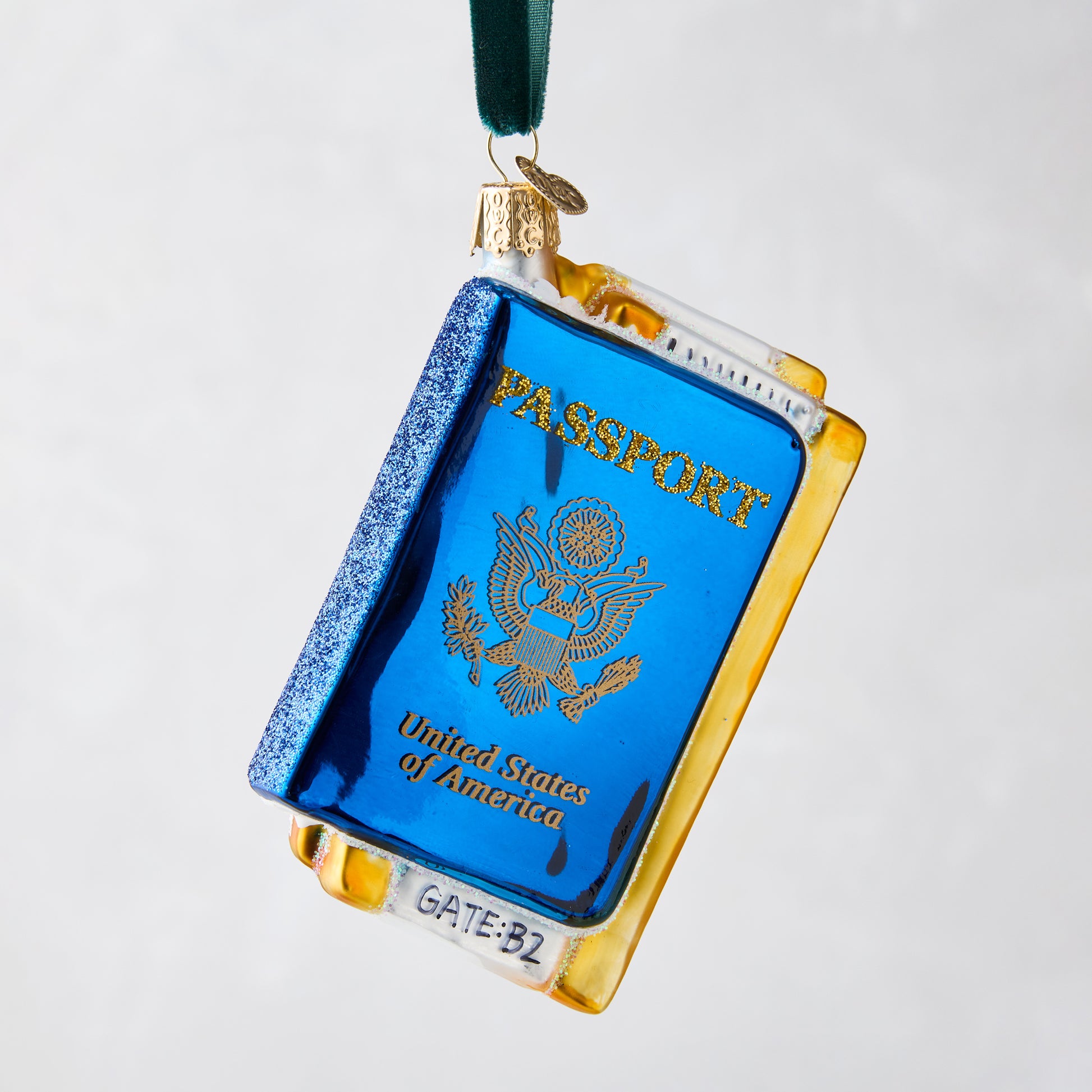 Hand-painted glass and resin Passport Christmas ornament, blue with gold details, hanging from a green ribbon.