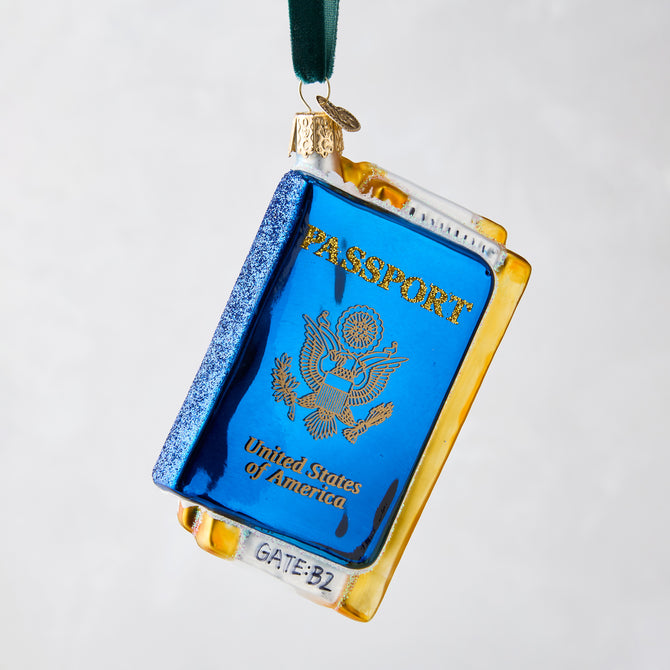 Hand-painted glass and resin Passport Christmas ornament, blue with gold details, hanging from a green ribbon.