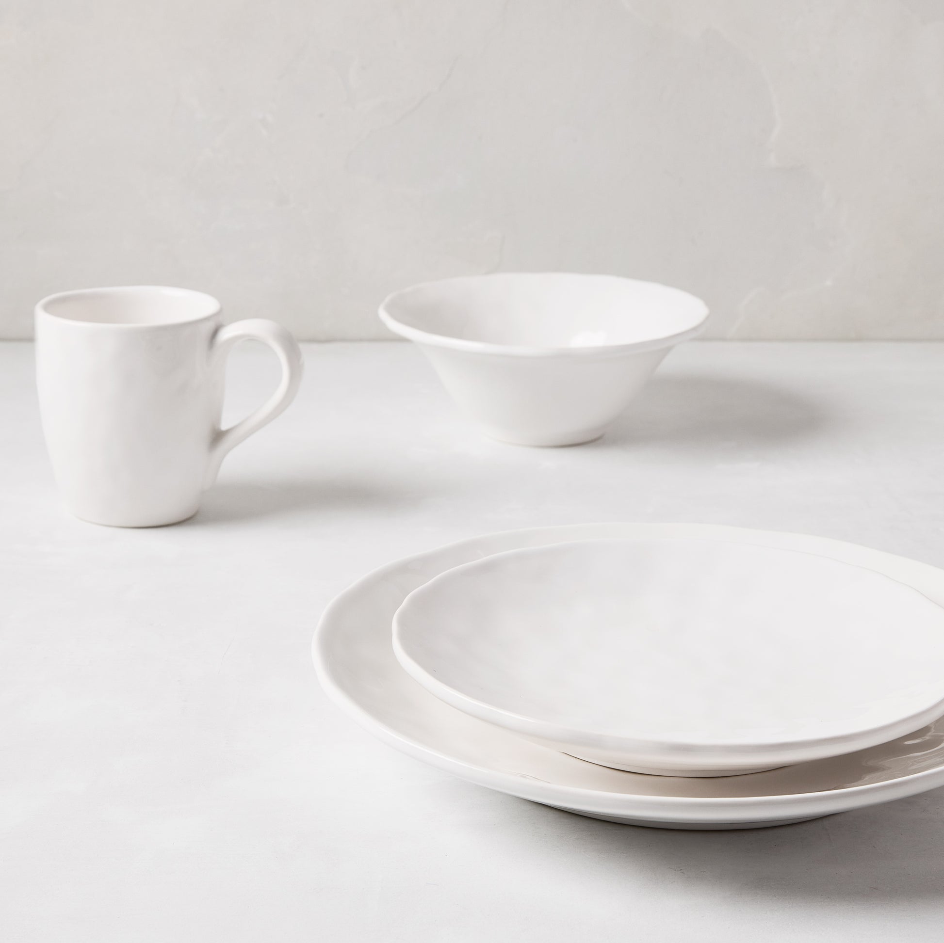 Pebble White ceramic mug, bowl, and two plates with subtle textures on a light background.