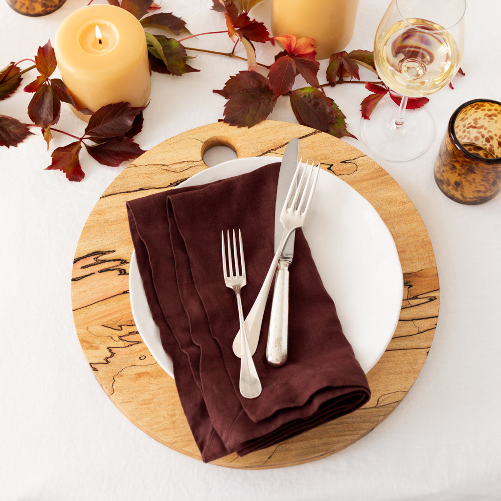 Pebble White ceramic salad plate on a round wooden charger with a brown napkin and silverware.