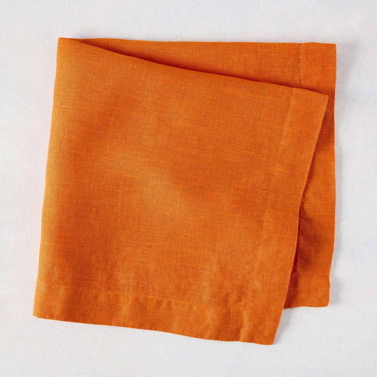Persimmon HG Signature hand-dyed orange linen napkin, 22-inch square, folded on a white surface.