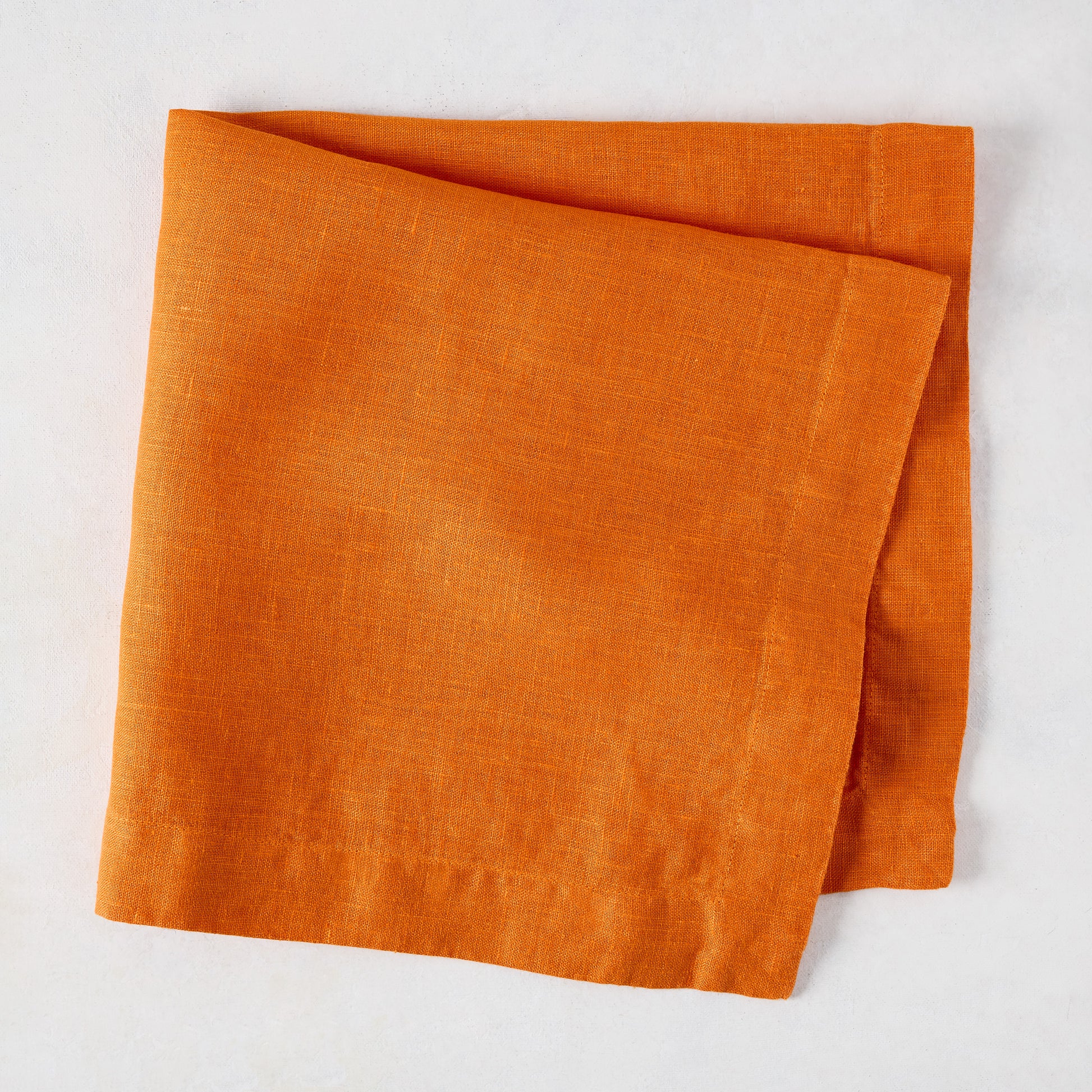 Persimmon HG Signature hand-dyed orange linen napkin, 22-inch square, folded on a white surface.